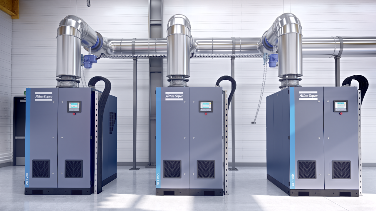 3 grey Atlas copco air compressors side by side, piped together into a silver header on a factory floor
